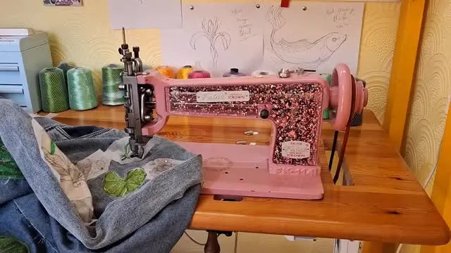 A close-up of a pink Falak chain stitch embroidery machine wearing a custom glittery acrylic faceplate.