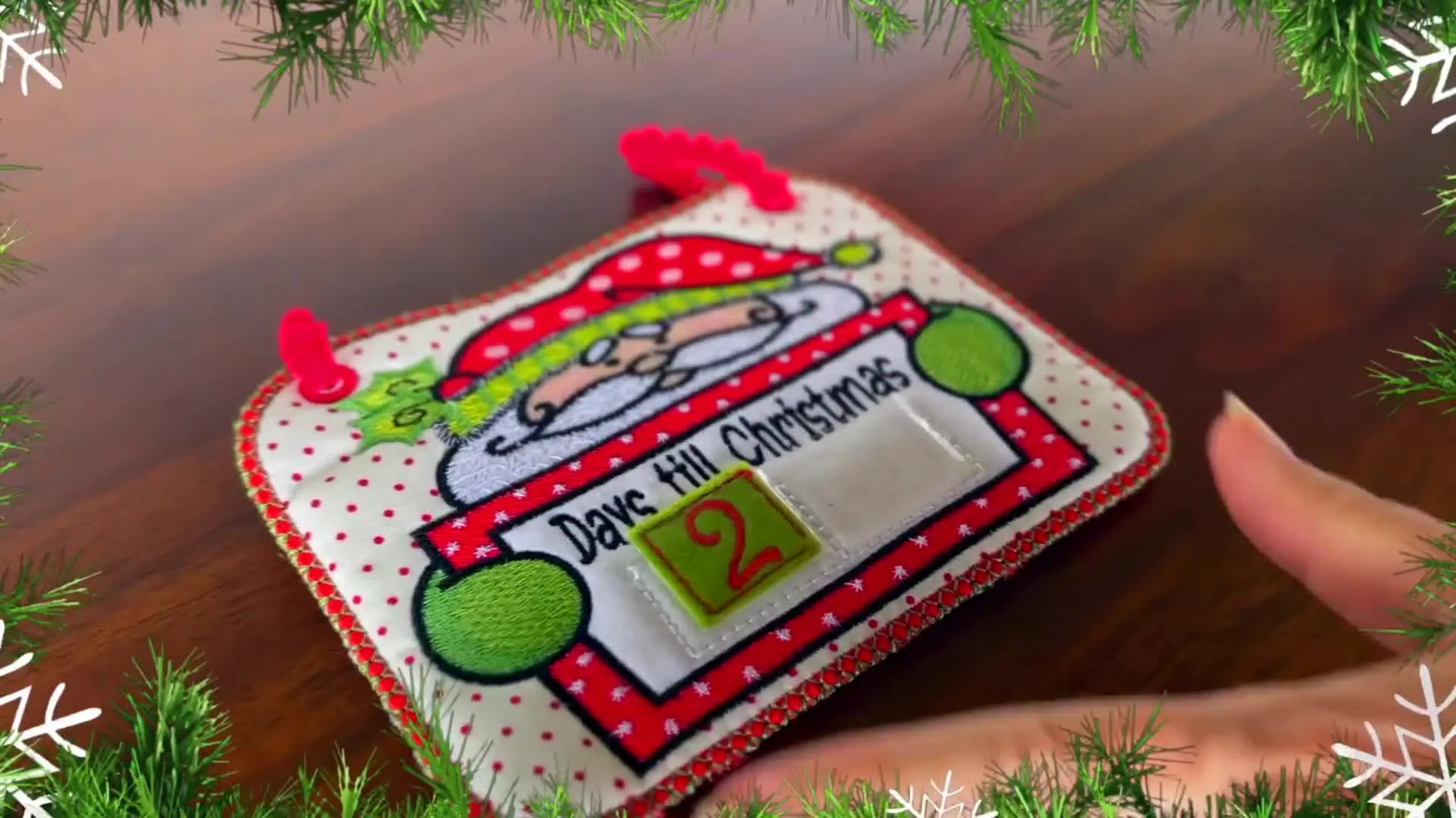 A close-up of the finished ITH Santa Countdown calendar as a hand places a felt number tile into the pocket window.