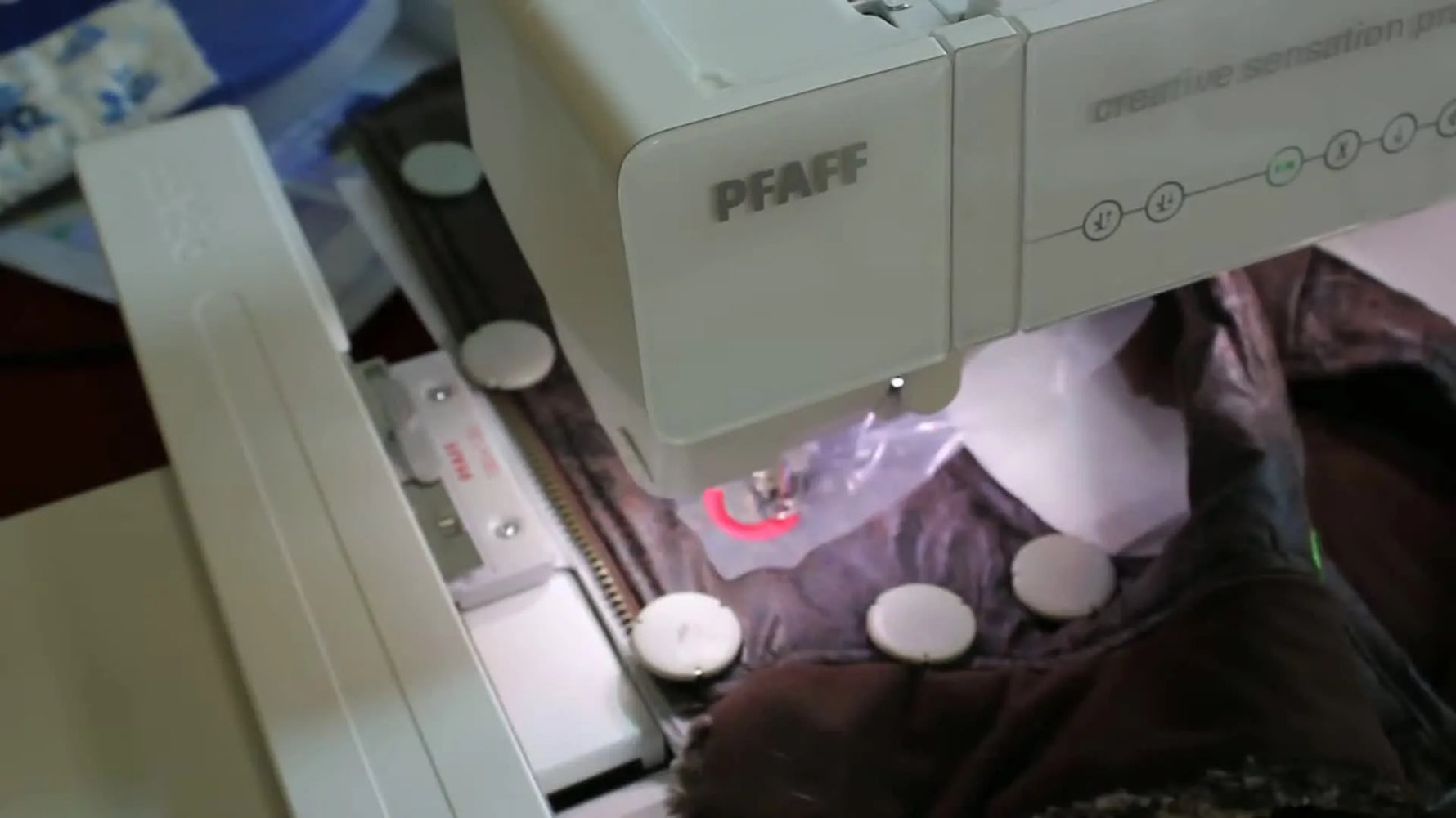 Close-up of strong round magnetic tabs holding a thick dog coat fabric securely on a Pfaff metal hoop.