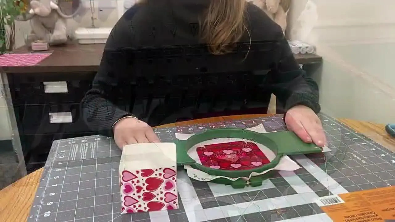 A close-up of the finished embroidered heart design stitched on patterned paper while still mounted in the hoop on the Tajima machine.