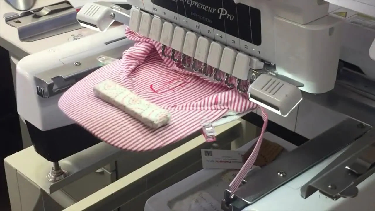 A close-up of the Brother PR1000e stitching the monogram tack-down outline in red thread on a hat mounted in a curved Fast Frame.