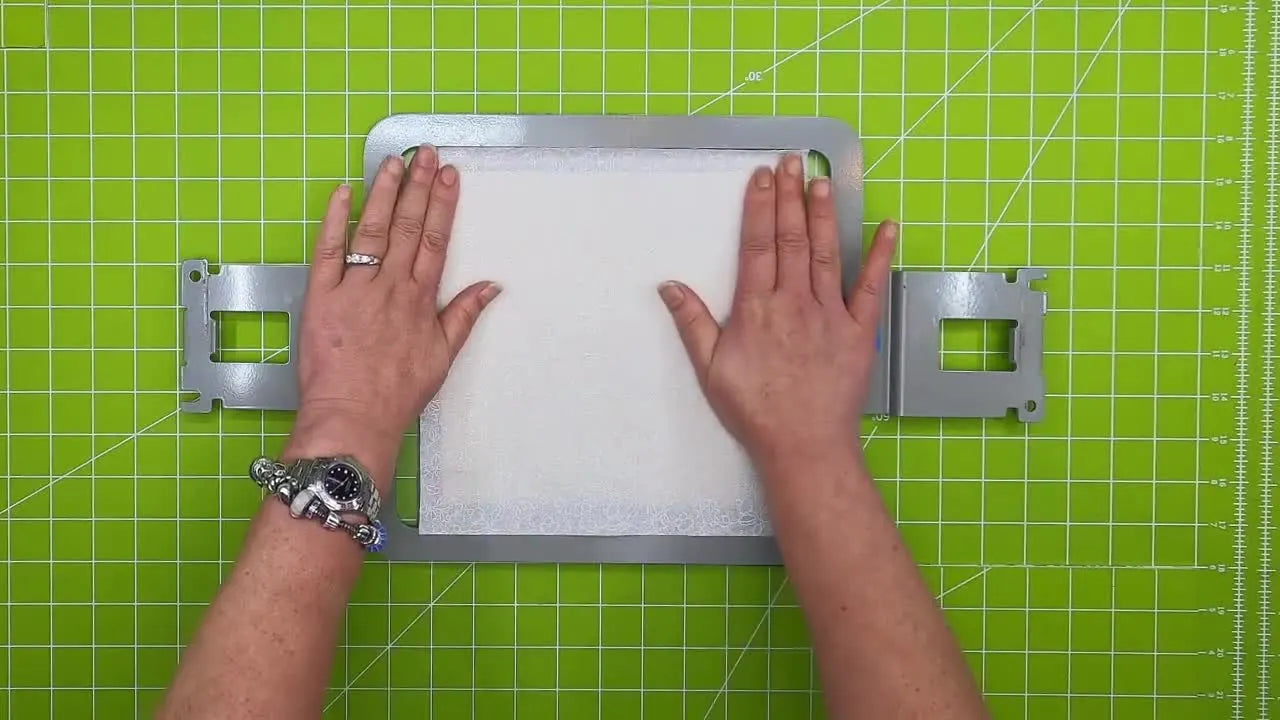 Hands smooth the quilt block from the center outward to bond the fabric layers to the double-stick tape inside the Monster Block Maker jig.