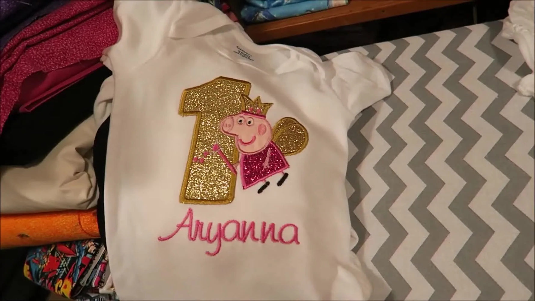 A finished embroidered onesie with a glitter appliqué number and a character design, shown flat from above.