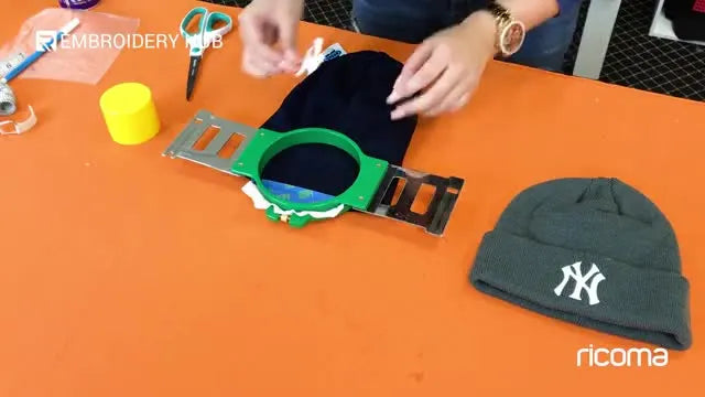 A paper placement template is temporarily stuck to a hooped beanie cuff to make centering easy even with painter’s tape in the way.