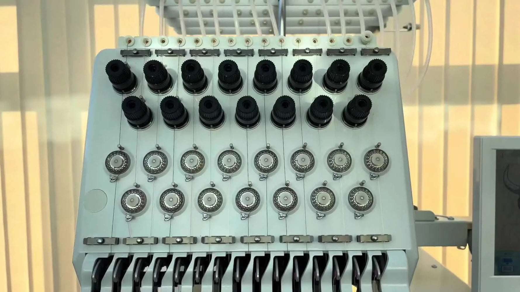 Close-up of the Happy Japan HCU embroidery head showing the 15 tension knobs and needle bar area where speed and stitch quality are won or lost.