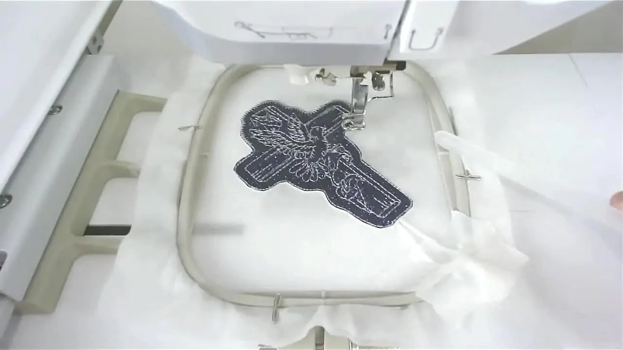A finished glitter Dove of Peace cross ornament is held up close, showing the sparkle and crisp satin border.