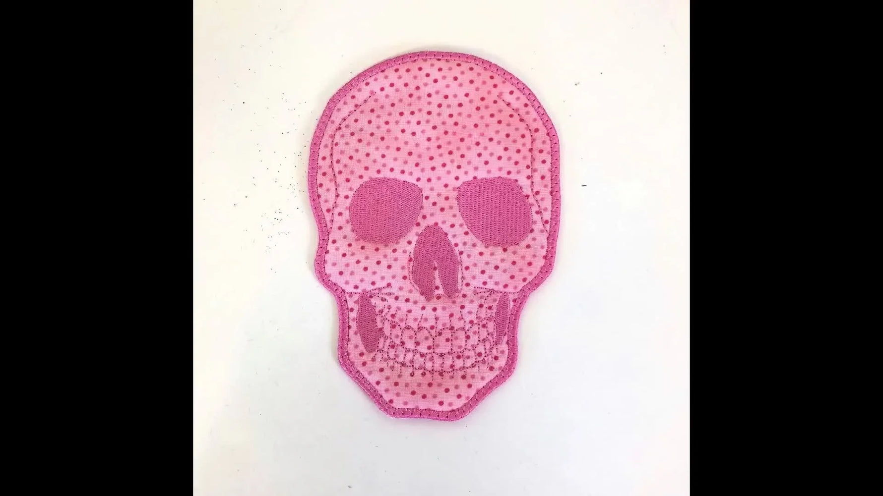 A finished pink skull coaster shown close-up with a clean satin-stitched edge.
