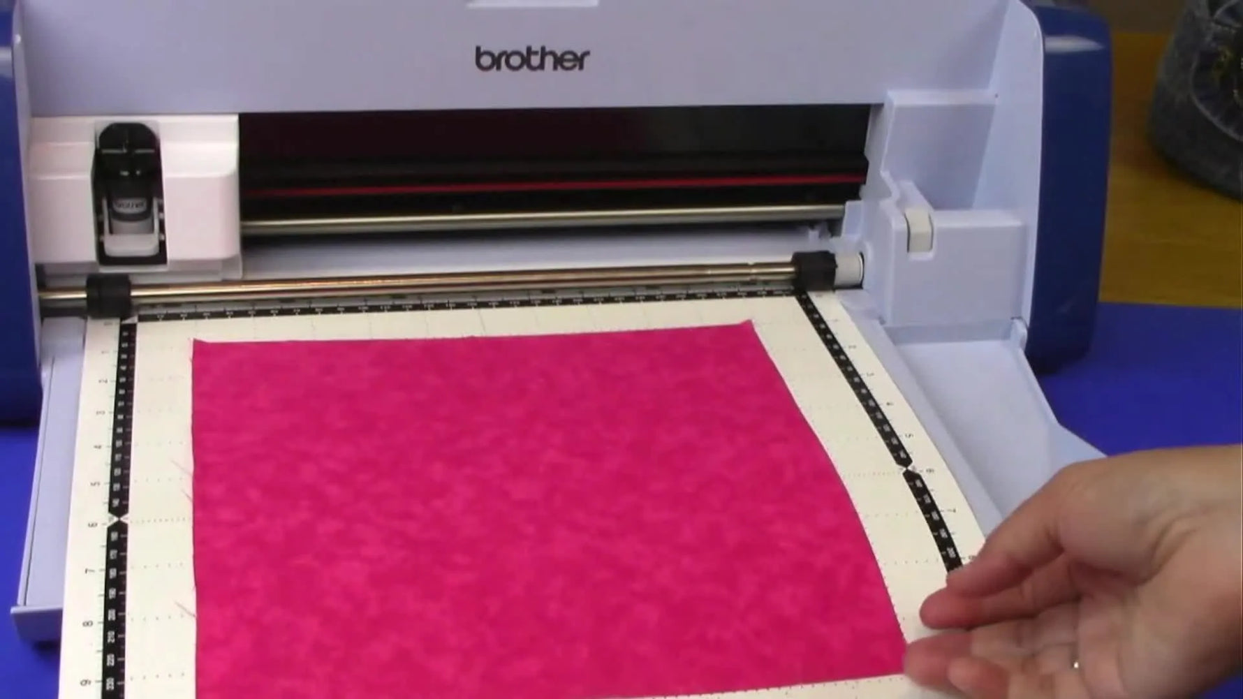 Hands place a precision-cut pink butterfly appliqué piece into the embroidery hoop, aligning it perfectly to the placement stitches.