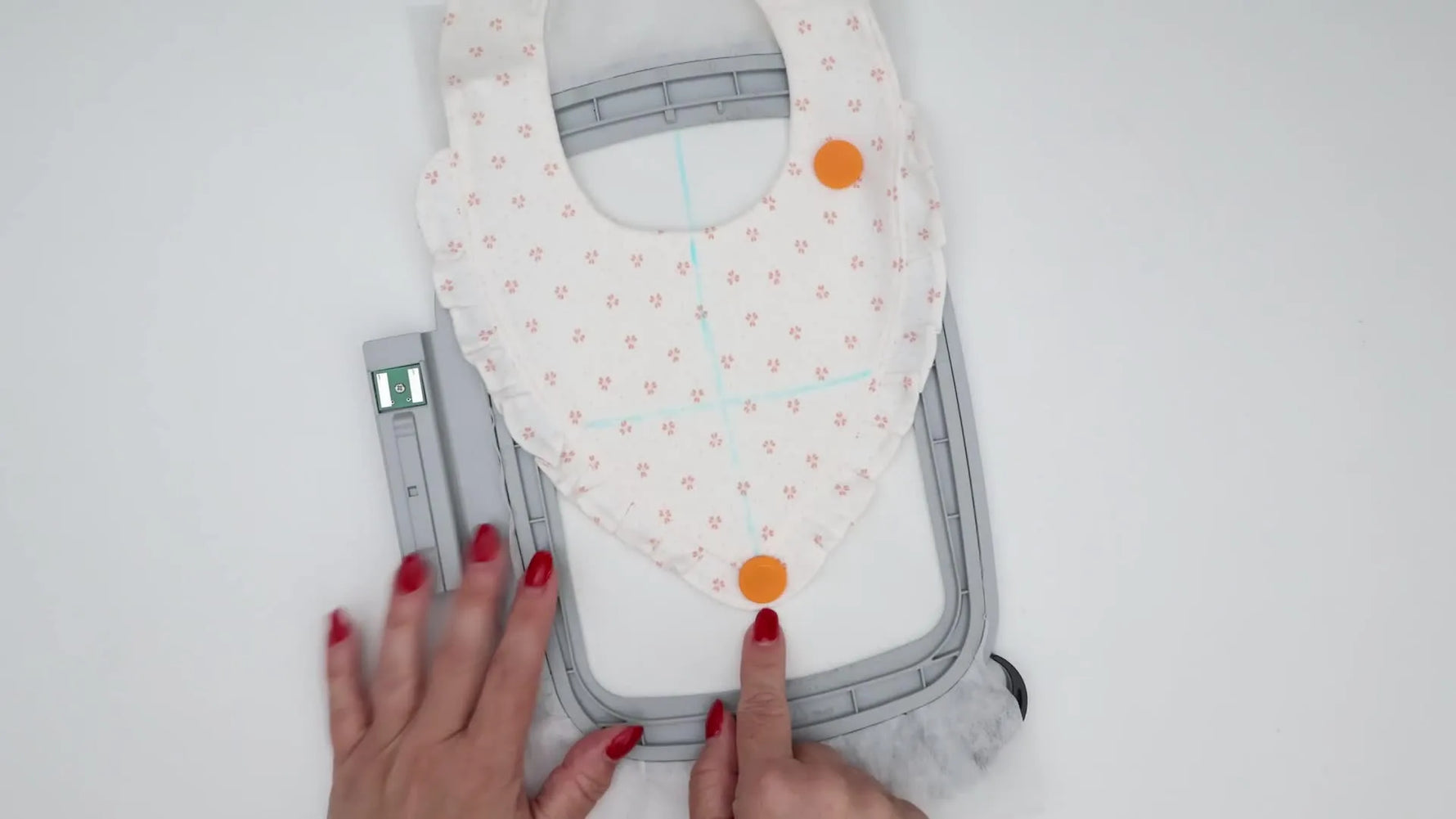 An overhead view of a baby bib floated on hooped stabilizer and held flat with multiple magnetic clips around the perimeter.