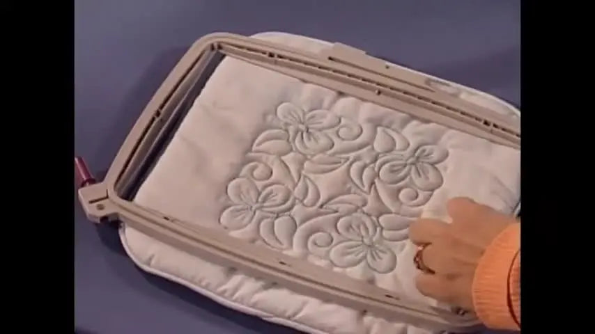 A thick quilted block is secured in a clamp-style specialty hoop to prevent hoop burn and slipping.