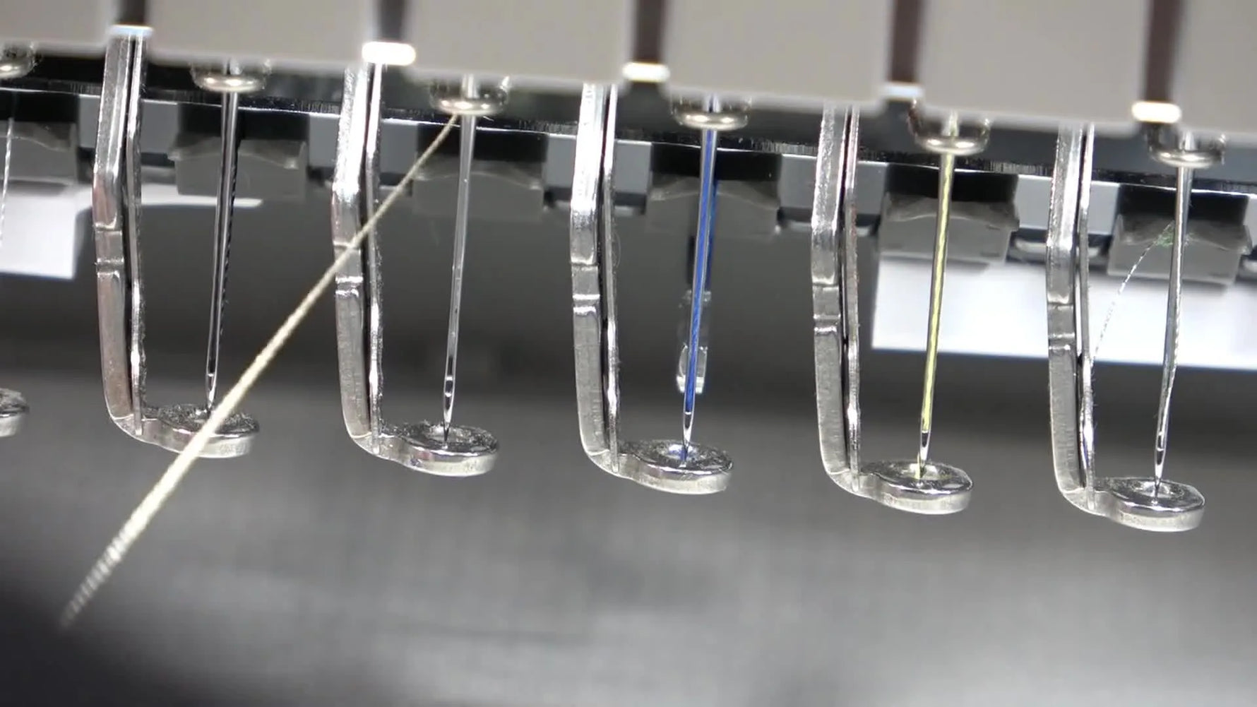 An extreme close-up shows the Brother PR1055X automatic needle threader hook passing cleanly through the needle eye.