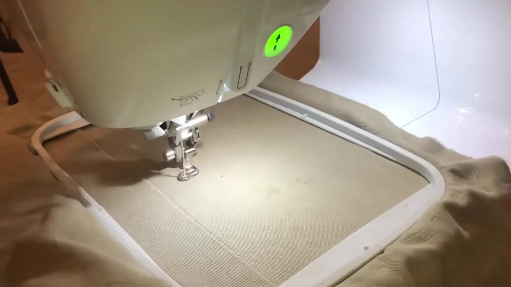 A close-up of the Brother PE800 actively stitching a SpaceX logo on beige fabric inside the 5x7 hoop.