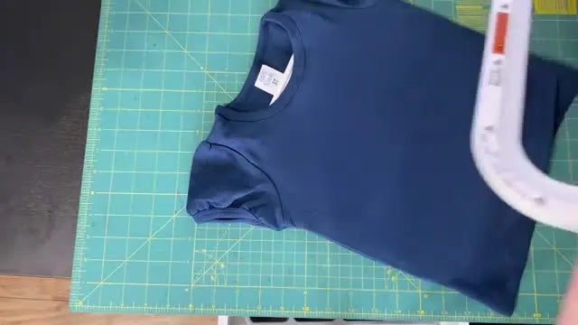 An overhead view shows the top magnetic frame being positioned with the warning label visible before it snaps shut over the hooped shirt.