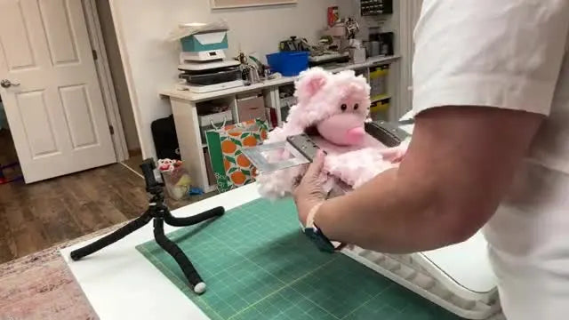 A hooped plush bear is lifted off the hooping station, showing smooth, even tension ready for stitching.