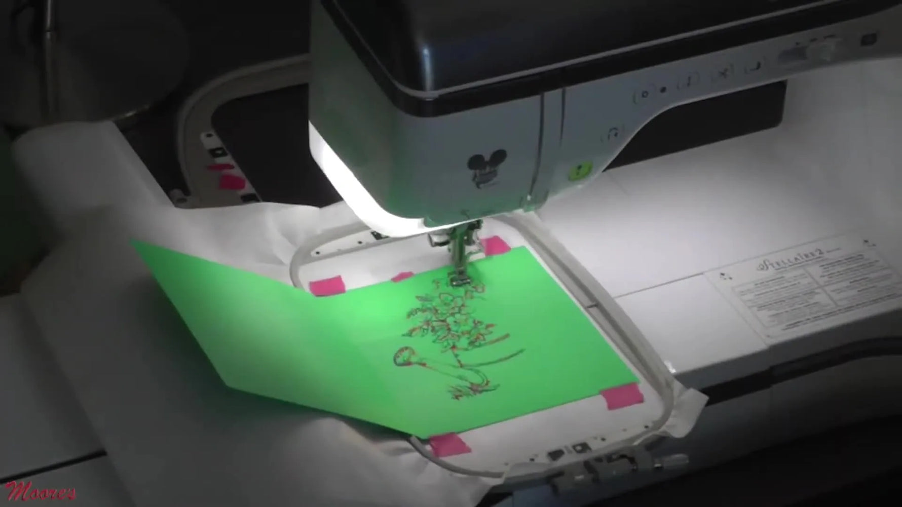 A close-up of a Brother Stellaire stitching a floral outline design onto green cardstock hooped over stabilizer.