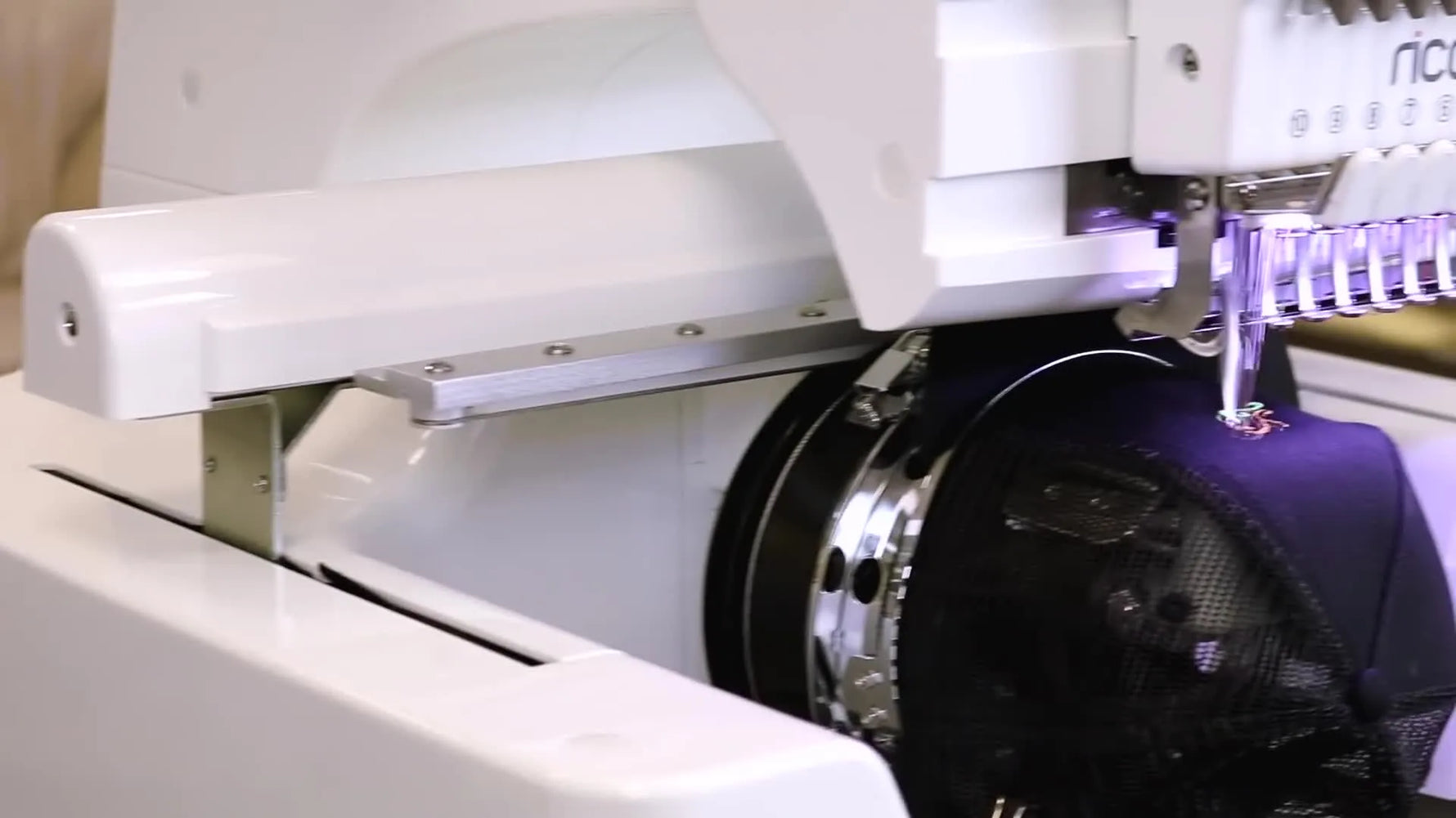 Close-up of the Ricoma EM-1010 stitching on a cap using the wide-angle cap driver system.