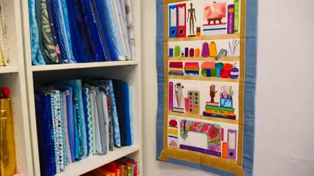A finished Crafty Shelves Hanger wall quilt displayed on the wall, showing crisp block joins, a centered hanger loop, and a clean stitched border.