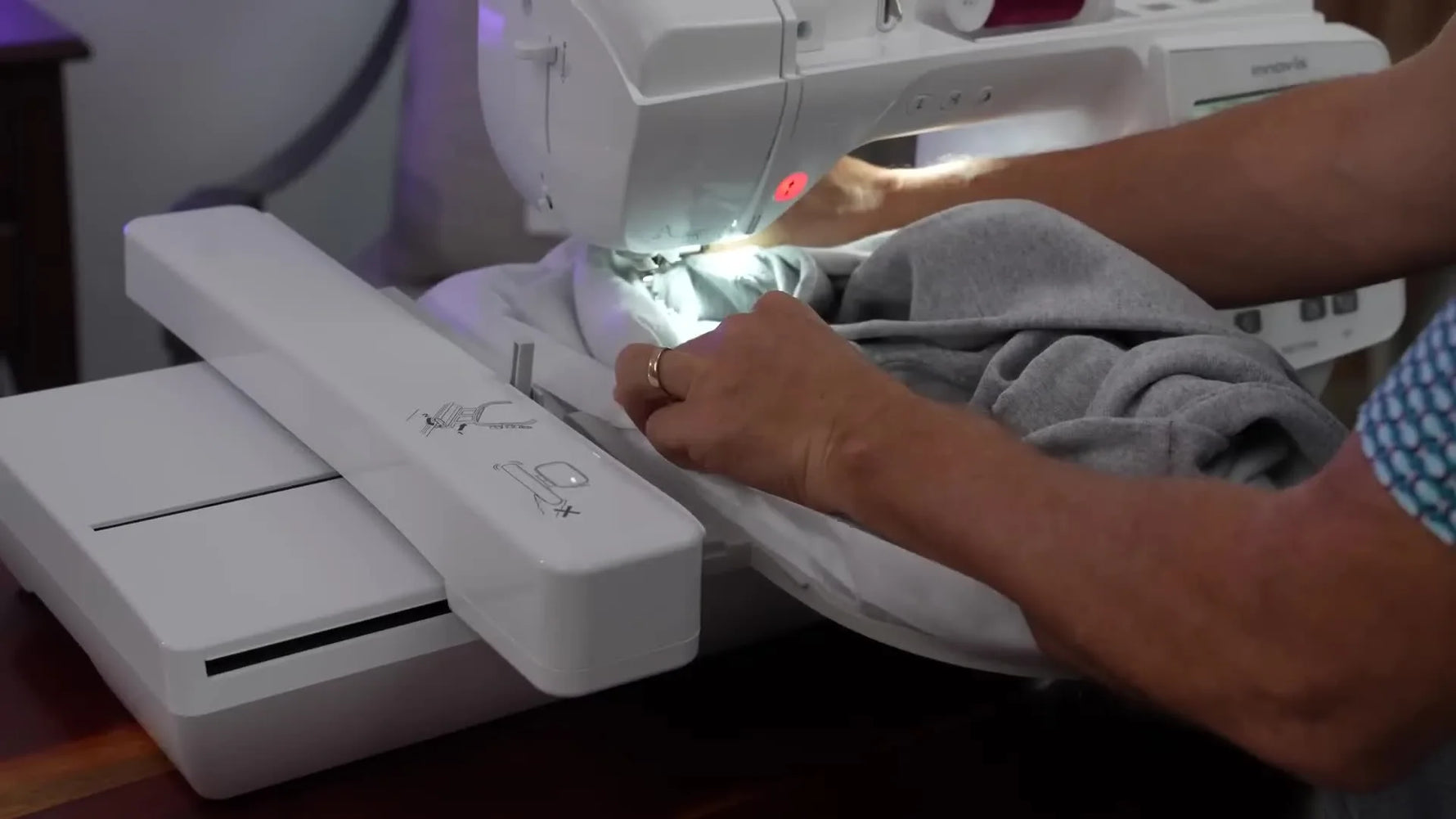 A sweatshirt is arranged into a controlled “bowl” around a flatbed embroidery machine so the needle area stays clear while stitching.