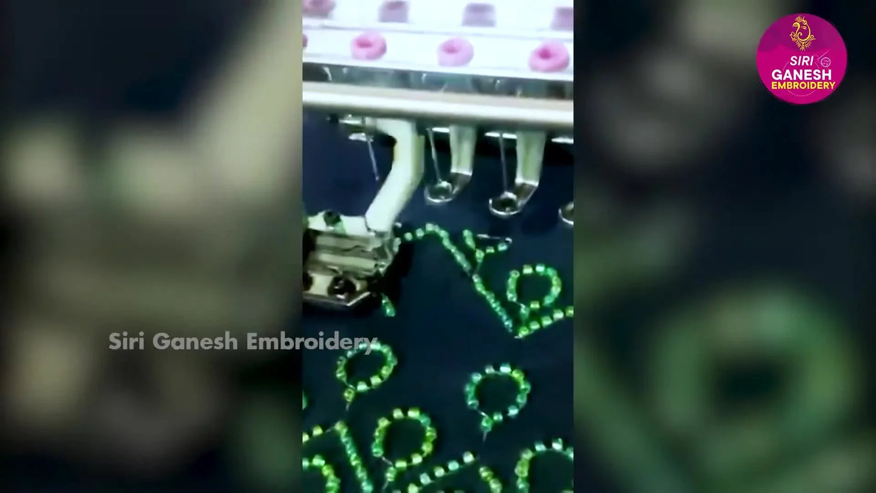 A close-up angled view of a 12-needle commercial embroidery head stitching a green geometric repeat on dark fabric while the needle bar reciprocates at speed.