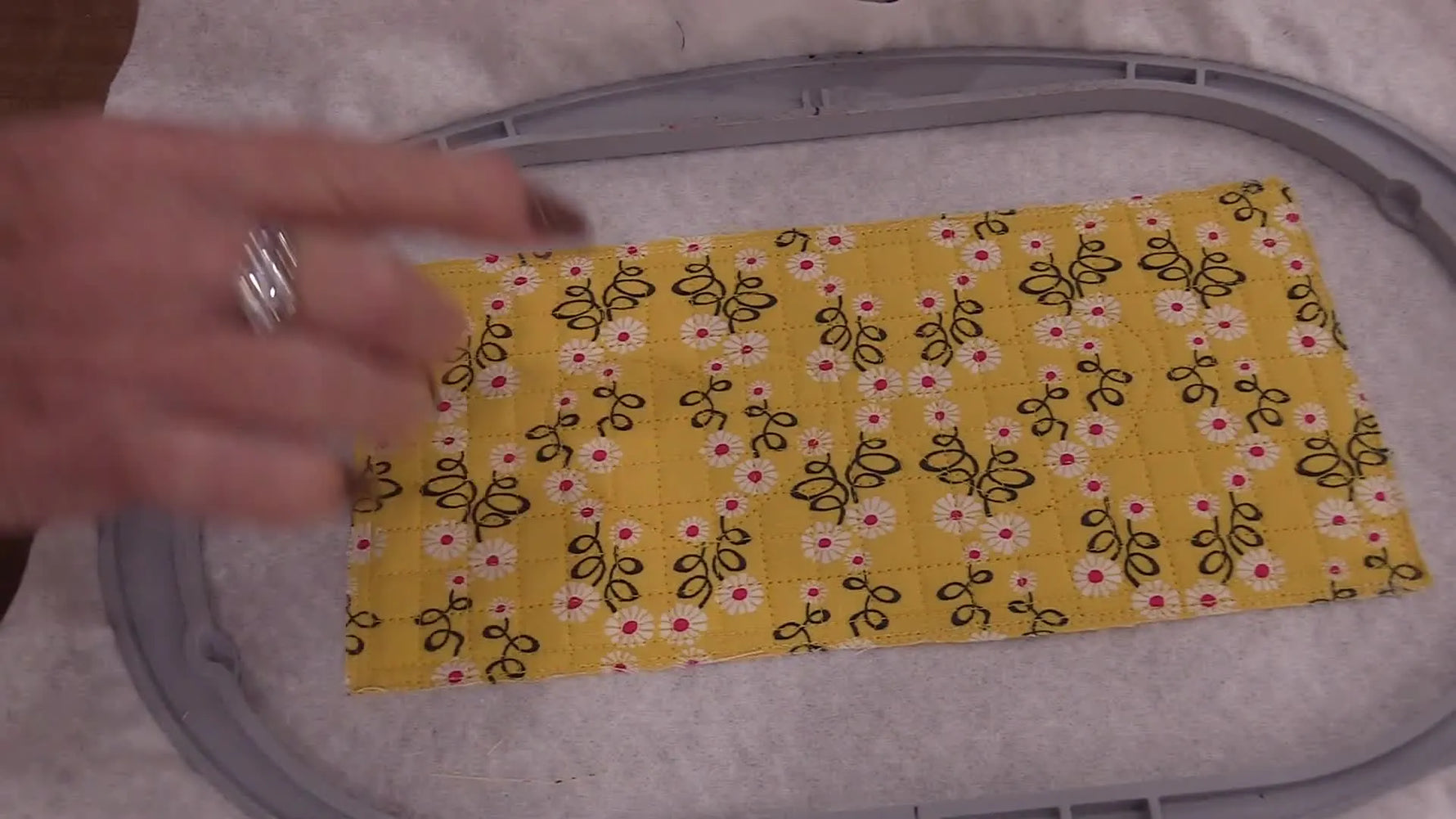 Overhead view of sparkly black Luxe Vinyl hearts being positioned on the quilted yellow front panel inside the hoop.