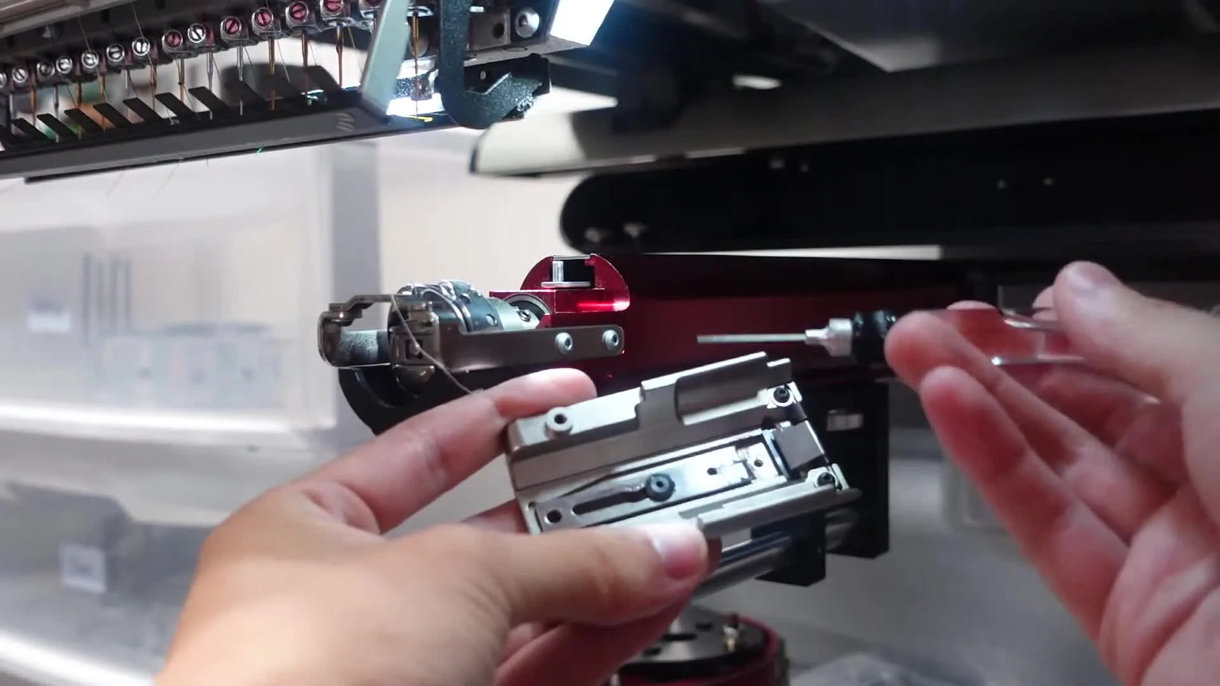 Close-up of oil being applied to the cutter knife pivot rivet on the removed needle plate during weekly maintenance.