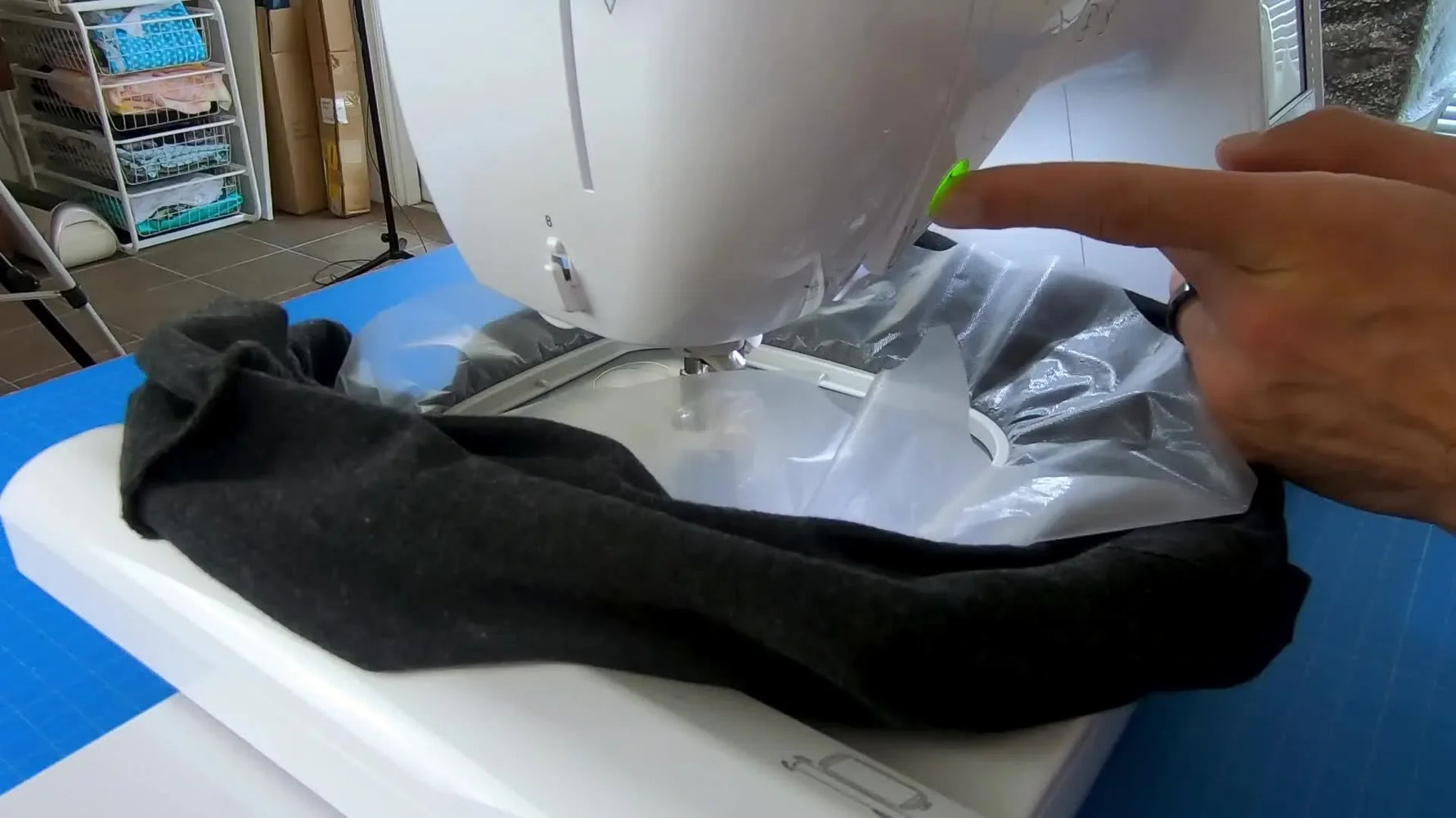 A close-up of the Brother PE800 needle stitching a bright design onto a black knit T-shirt through a clear water-soluble topper.