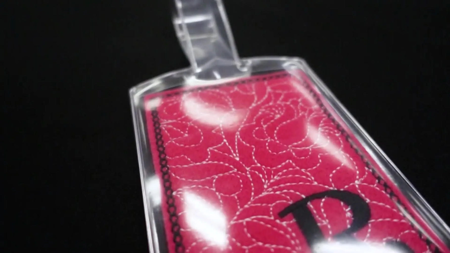 A finished pink felt luggage tag neatly inserted into a vinyl luggage tag holder, shown close-up on a dark background.