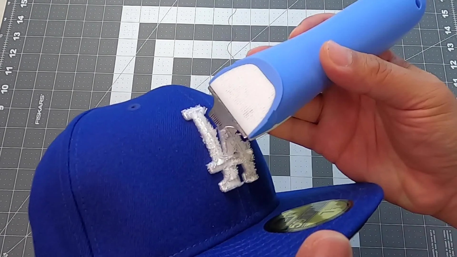 A close-up of an electric stitch remover shaving fuzzy thread off a 3D puff foam embroidery area to reveal the structure underneath.