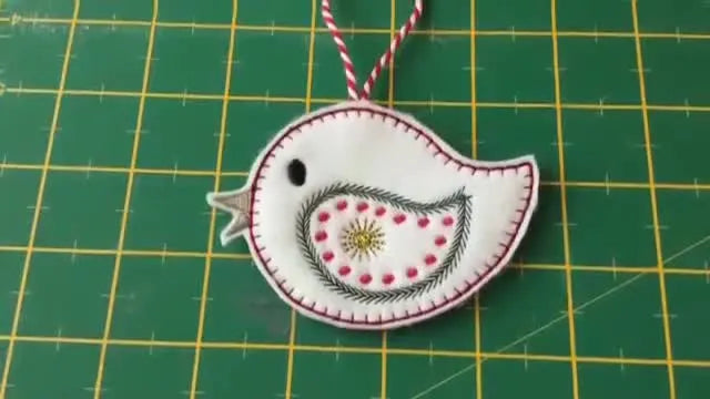 A close-up of the finished white felt bird ornament with red blanket stitching and a ribbon hanging loop.