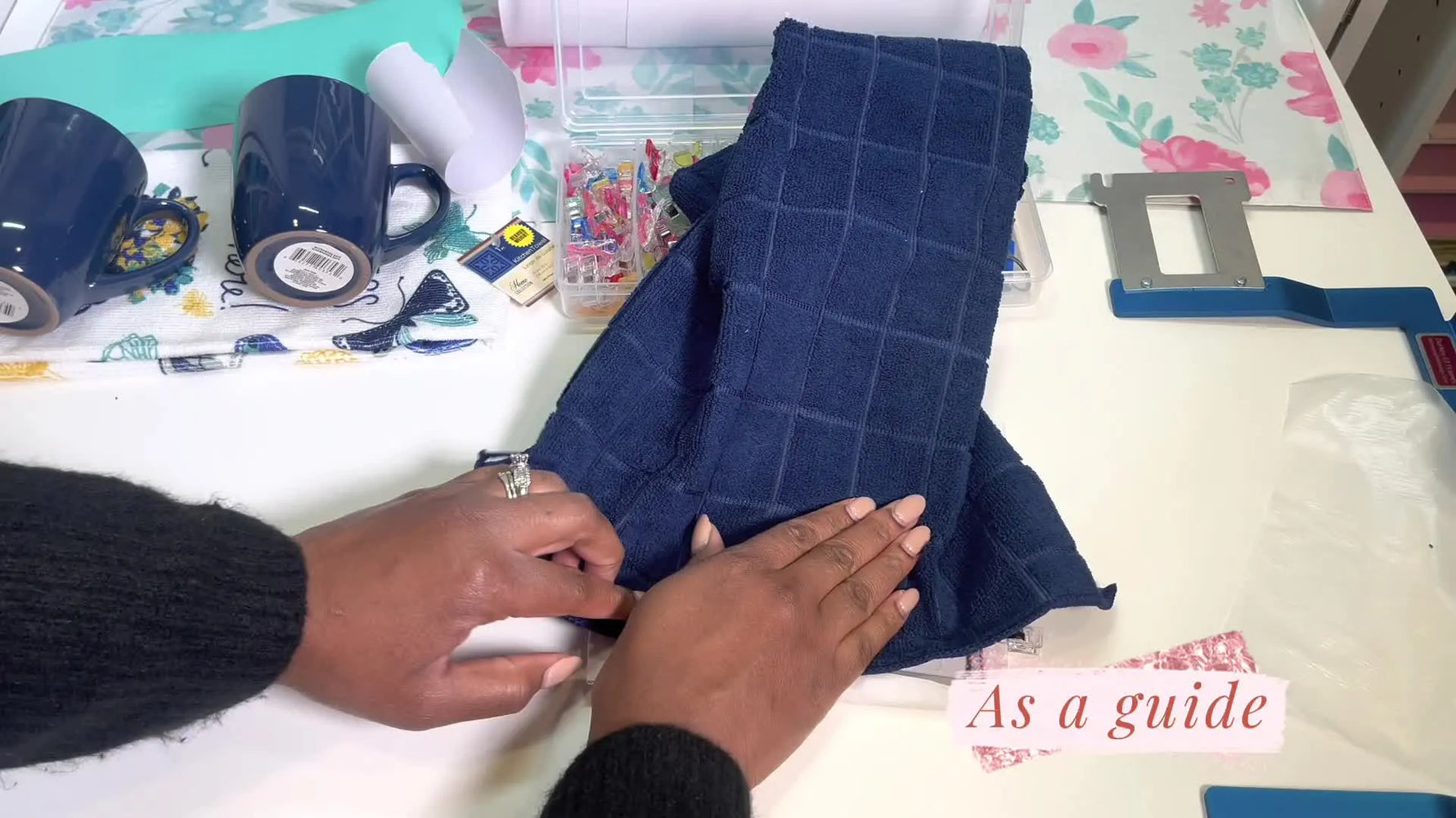 An overhead view shows a navy waffle-knit towel being pressed onto sticky stabilizer inside a Durkee-style frame for floating embroidery.