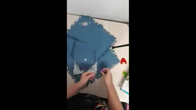 A blue napkin is floated over hooped stabilizer and secured with purple magnetic pins for precise embroidery placement.