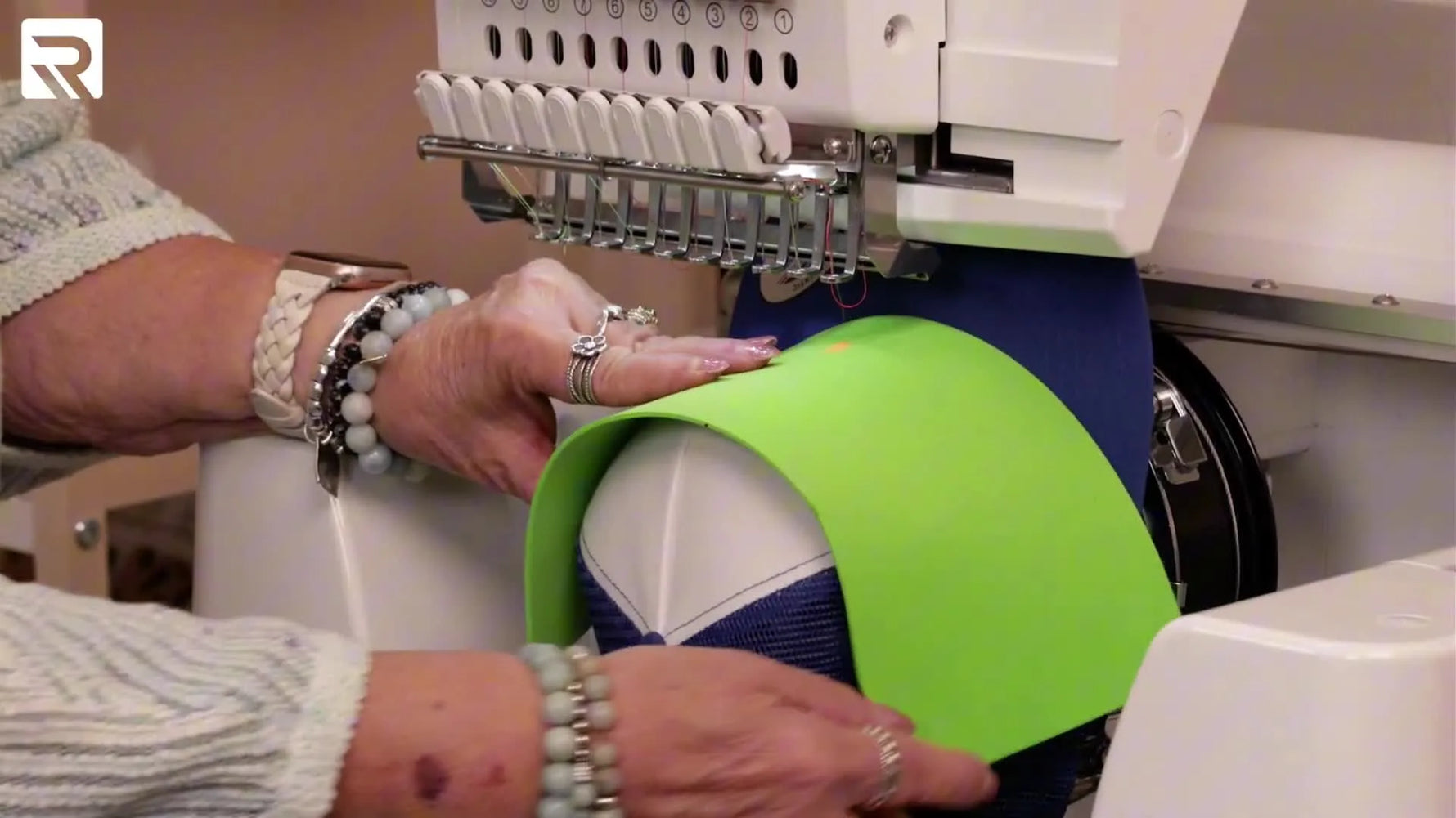 A close-up shows a spare needle pinning bright green puff foam onto a curved hat front to keep the foam from shifting during stitching.