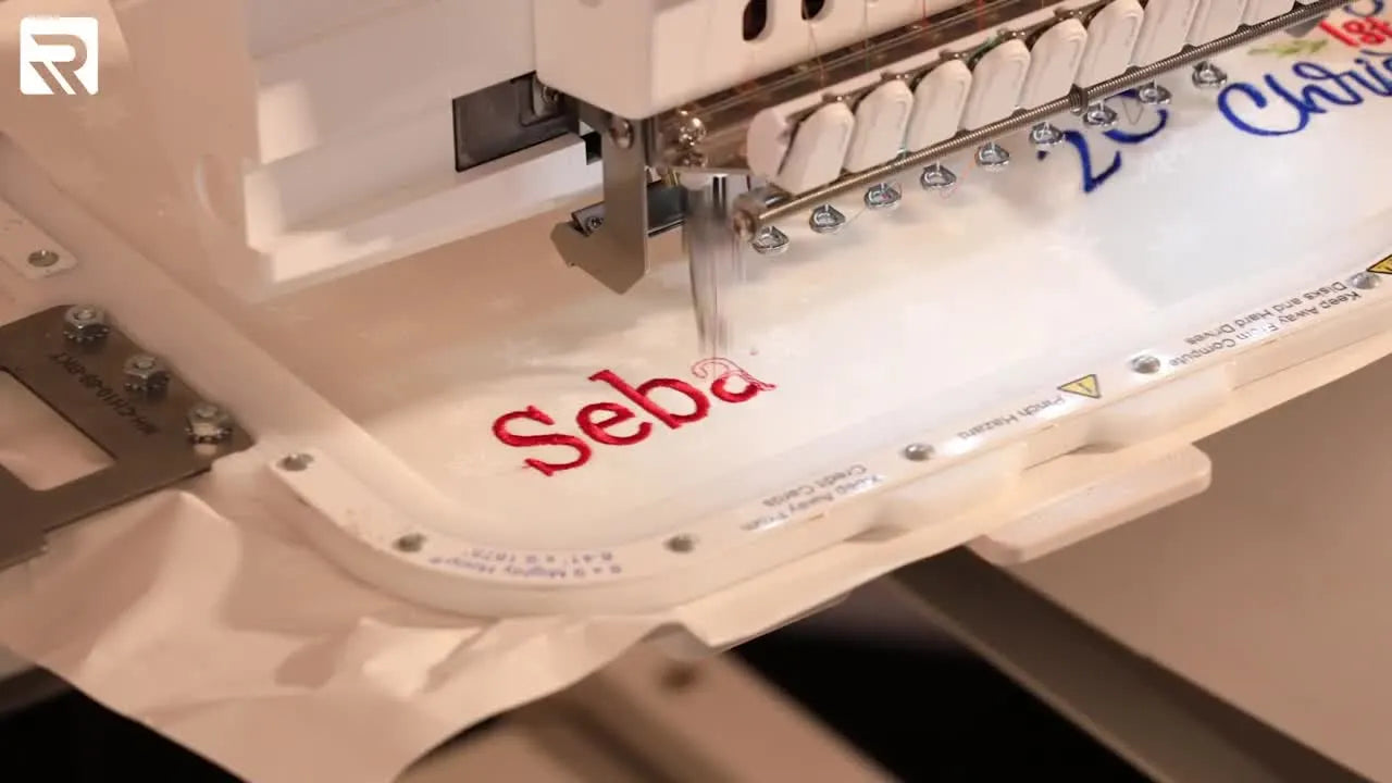 A close-up of the embroidery machine stitching a name in red thread while the cuff is floated on sticky stabilizer inside a magnetic hoop.