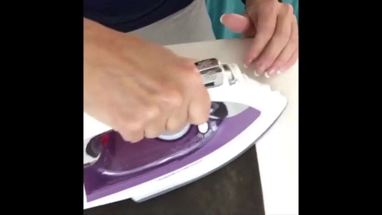 An overhead view of an iron pressing fusible Poly Mesh onto a knit T-shirt scrap to create a stable, soft embroidery base.