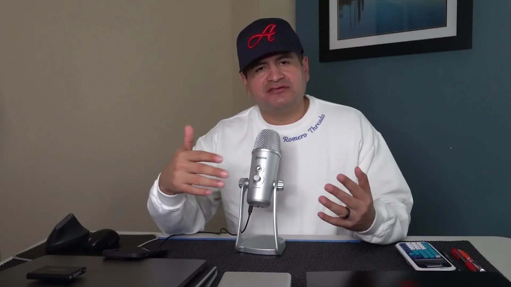 The host sits at a desk introducing the first essential for starting an embroidery business: choosing the right embroidery machine.