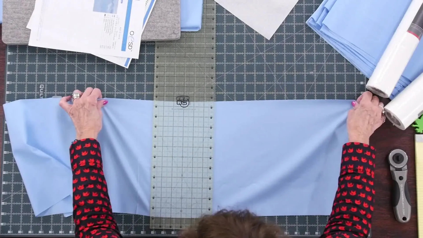 An overhead view shows a long quilting ruler aligned on fabric for a precise cut—exactly the kind of accuracy you need before stitching 32 tiling-scene blocks.
