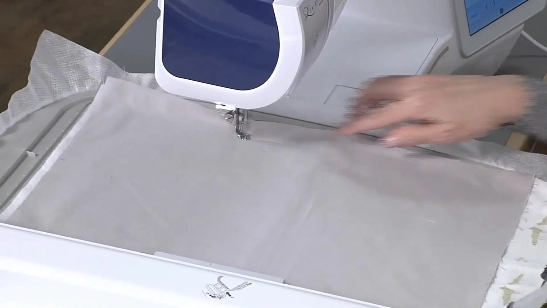 A wide shot of the embroidery machine stitching the final outline seam on the wrong side of the fabric during the ITH construction step.