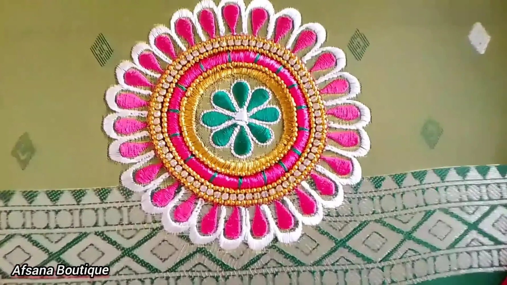 A wide view of the finished blouse back neckline showing repeating circular motifs with gold zari rings, a rhinestone chain border, pink fills, and a green center flower.