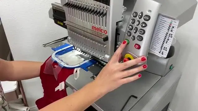 A close-up action shot of the embroidery machine stitching a name onto a plush stocking cuff inside a magnetic hoop.