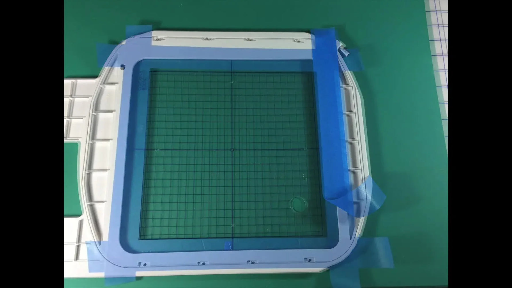 An overhead view shows blue painter’s tape aligned precisely on a Janome SQ23 hoop with the grid inserted, setting up the tape-float quilting method.