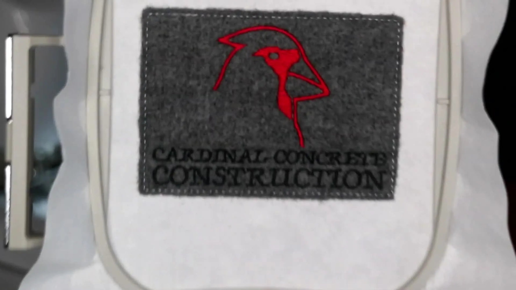 A finished grey felt patch is shown still in the hoop, with crisp black text, a red bird logo, and a clean satin border.