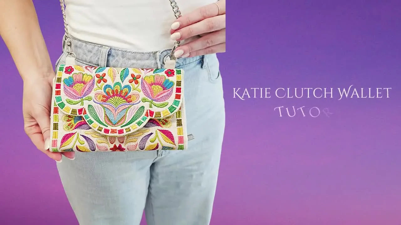 A finished embroidered Katie Clutch Wallet is held up with its chain strap, showing the final shape and hardware placement.