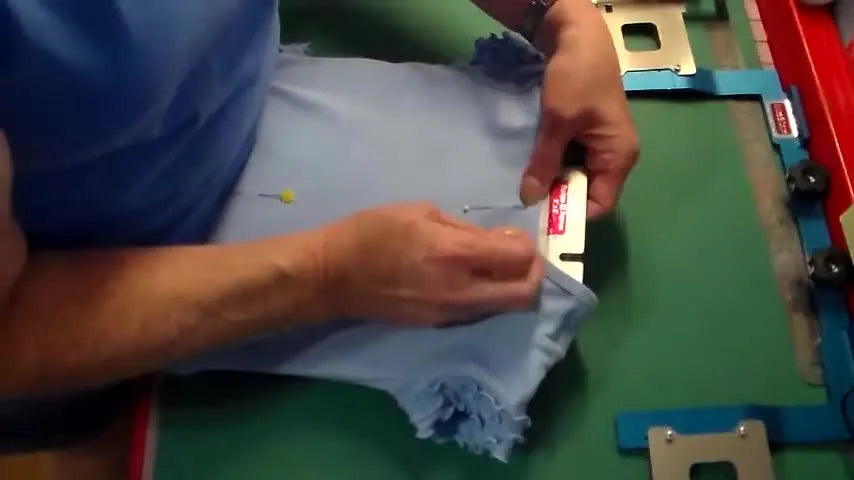 A child’s t-shirt is pinned at the neck center to a prepared frame, showing the alignment method before clipping and mounting.
