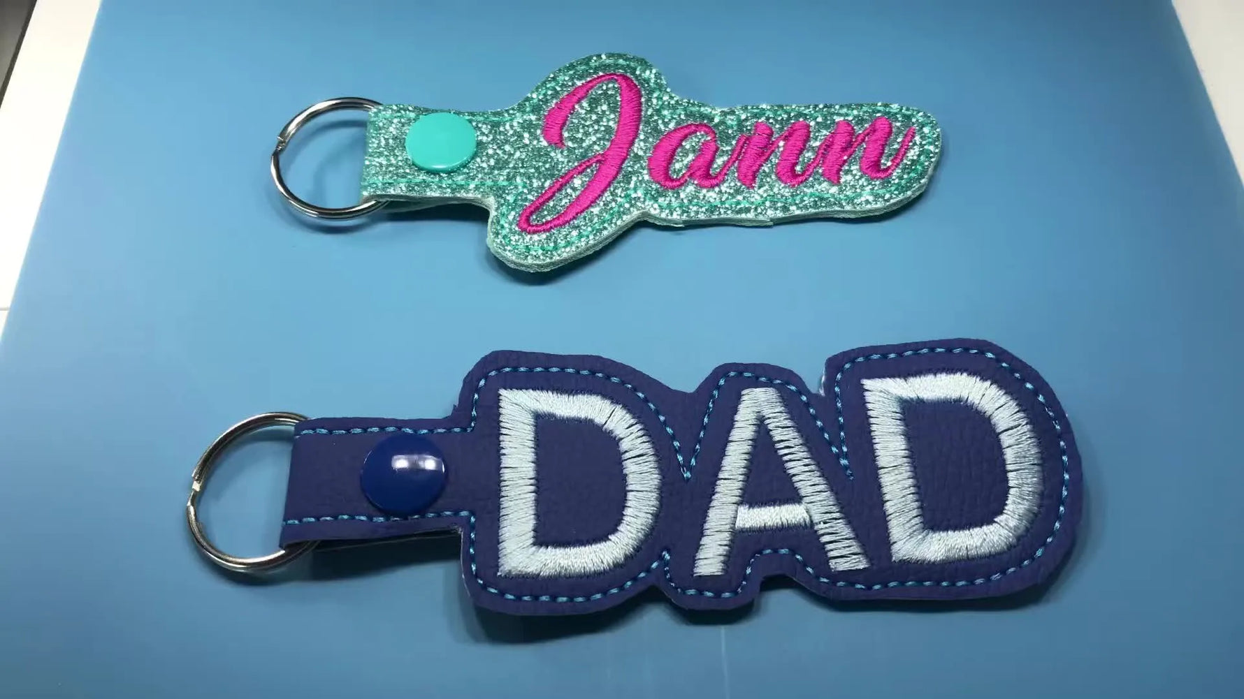 A set of finished ITH key fobs in glitter vinyl and embroidery leather, including a bold “DAD” version with snaps and D-rings.