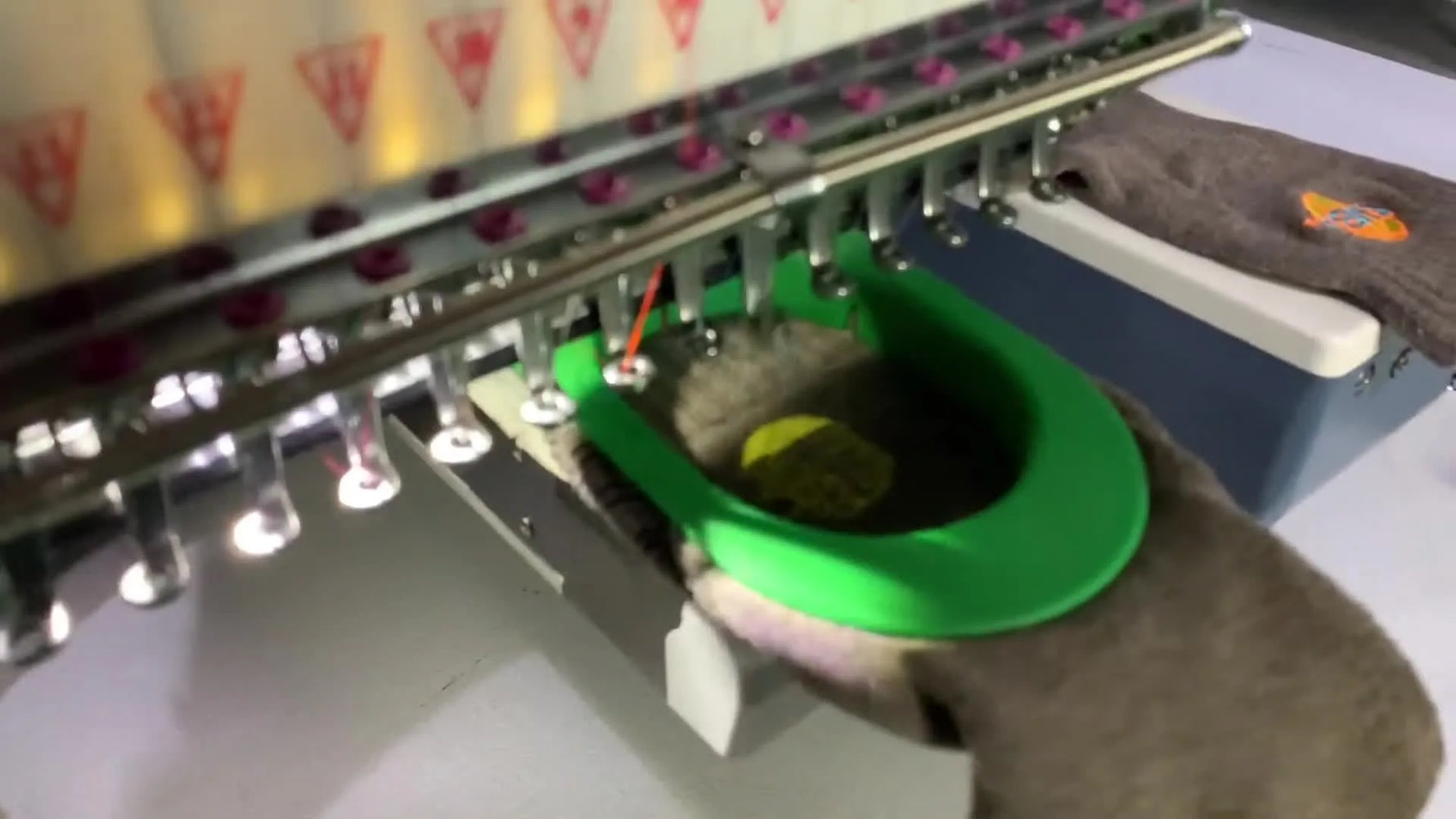 A YunFu single-head machine stitches an orange logo onto a sock held tight in a green clamping frame on the sock driver unit.