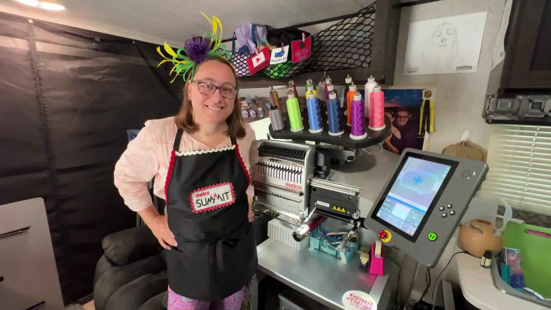 The instructor stands beside a Melco Summit embroidery machine with colorful thread spools, introducing a wireless file-sharing workflow.