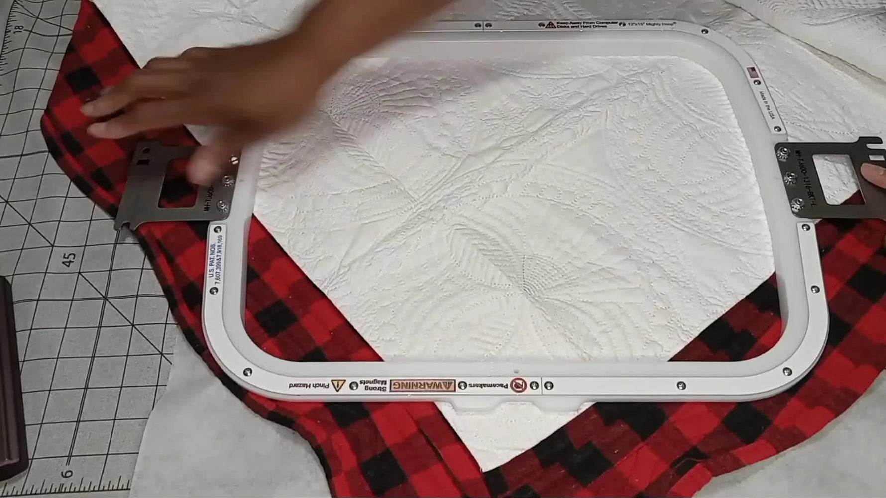 Hands clamp a thick quilted blanket and stabilizer sandwich as a 12x15 magnetic hoop snaps into place for a clean, fast hold.