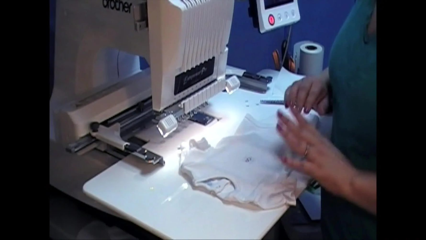 Close-up of hands smoothing a baby onesie onto a Fast Frame with sticky stabilizer for accurate centering before stitching.