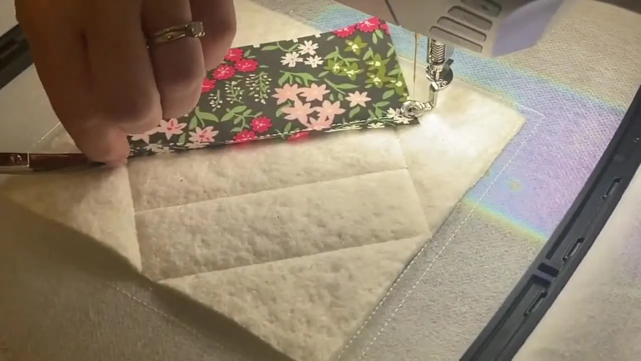 Close-up of double-curved embroidery scissors trimming fabric precisely along the in-the-hoop tack-down line.