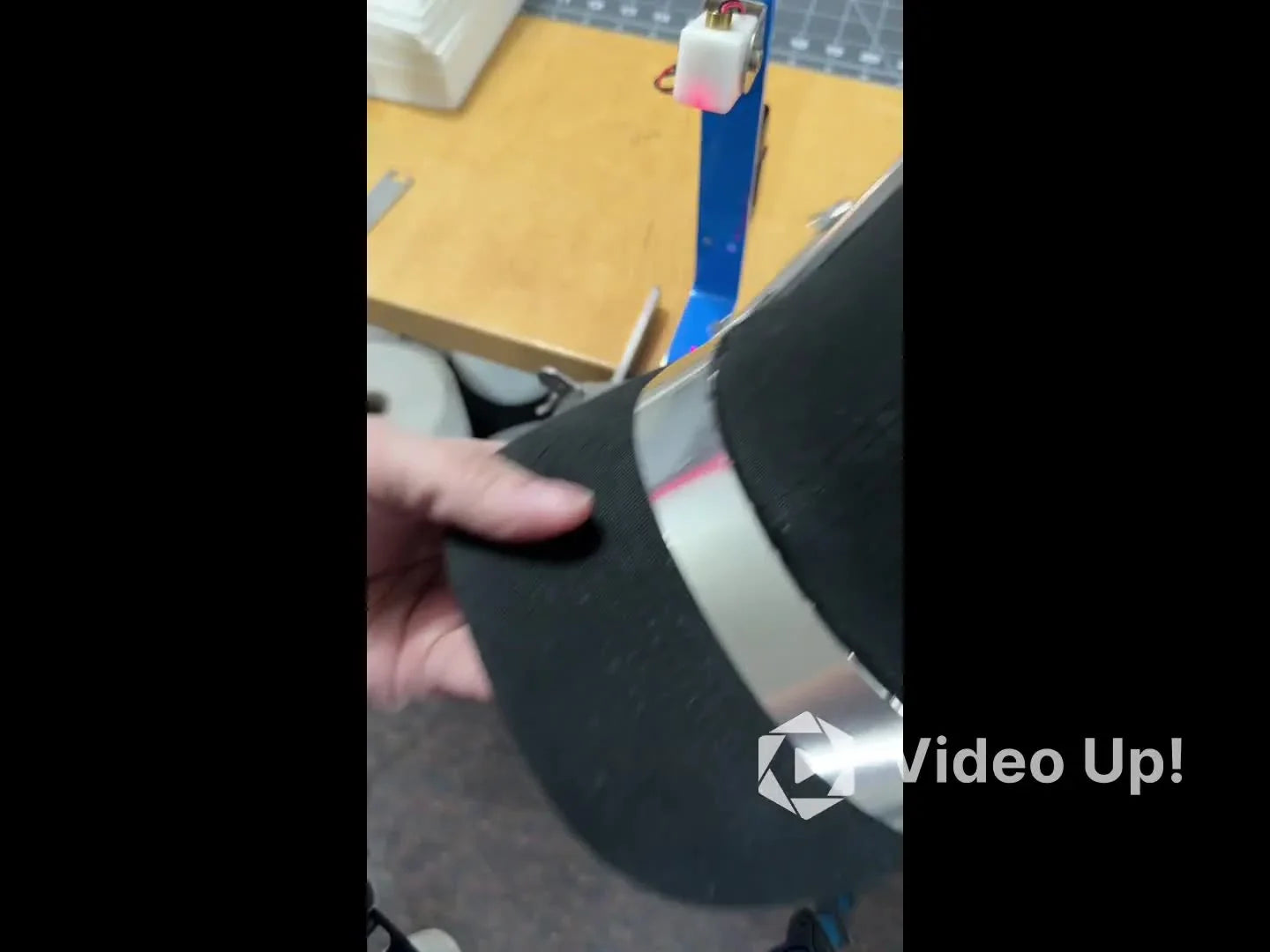 A side view of an unstructured dad hat hooped on the HoopTech Gen 2 cap frame, showing the back support plate holding the floppy crown steady.